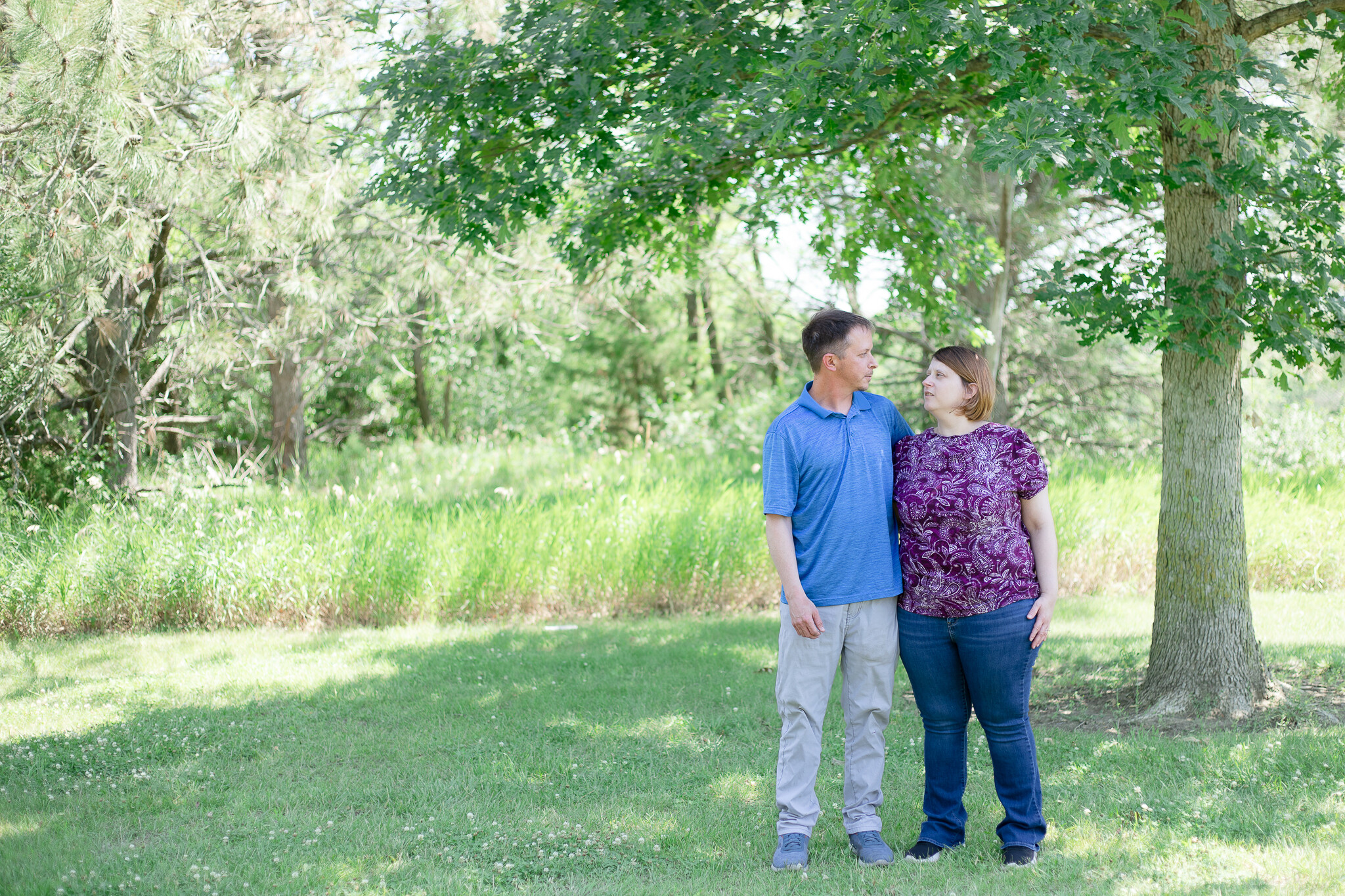 Couple standing under a tree smiling at one another, by an Omaha wedding photographer