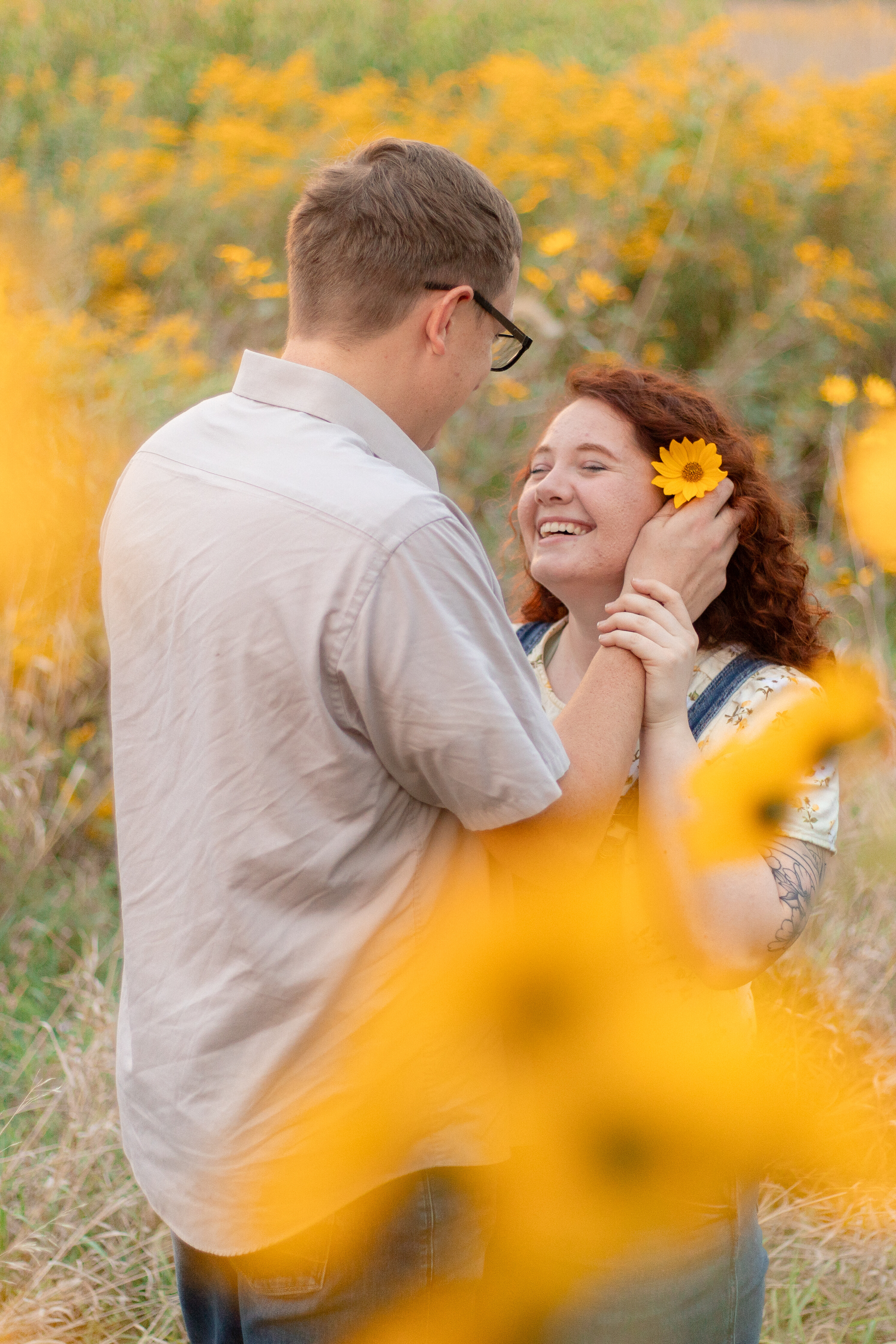 Girl smiling up at a boy putting a flower behind her ear during engagement photos in Omaha